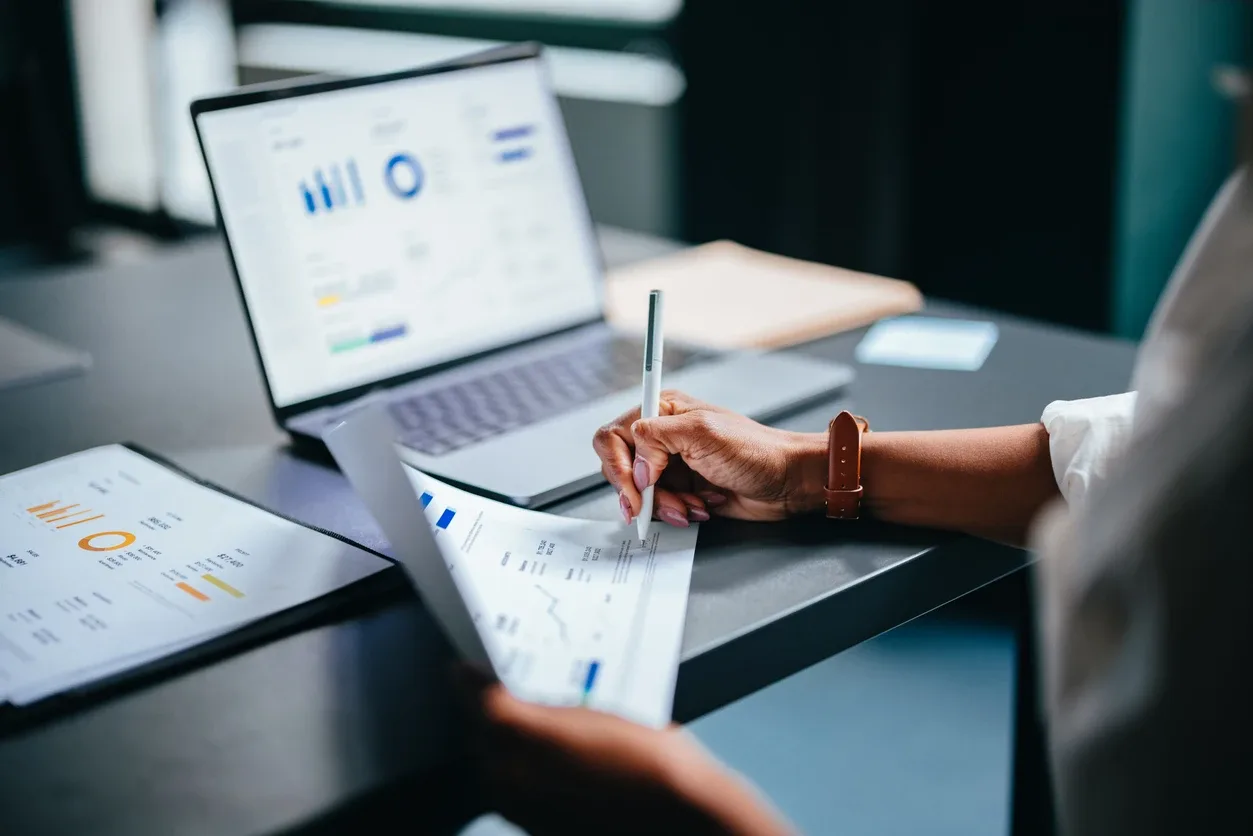 Cobrança recorrente: mãos analisando relatórios e gráficos financeiros em laptops no escritório, com assinatura em planilhas e dados de desempenho visíveis na tela