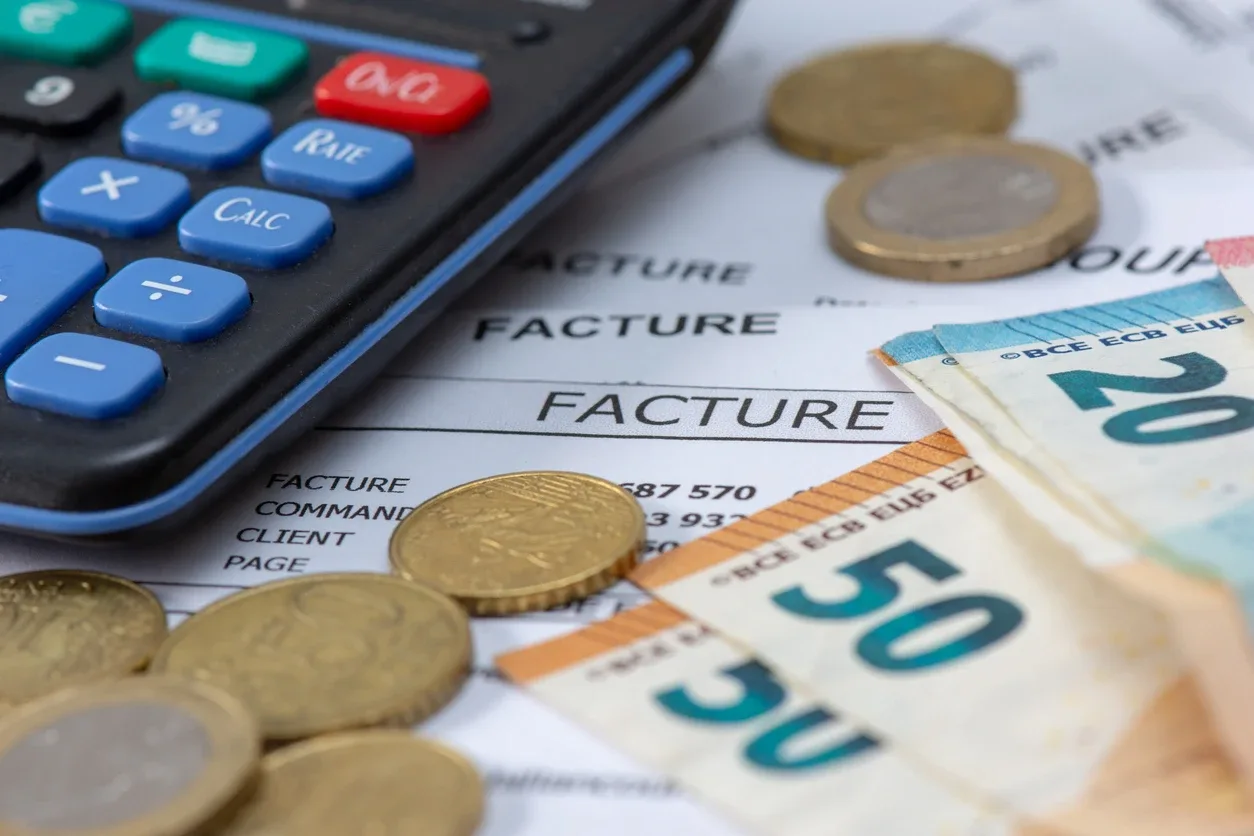 Melhores contas PJ: Calculadora ao lado de documentos de fatura, com moedas e cédula de 50 reais sobre papel, representando planejamento financeiro e contas empresariais.